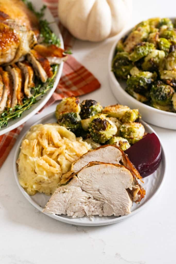 A plate of sliced turkey with mashed potatoes, Brussels sprouts and cranberry sauce.