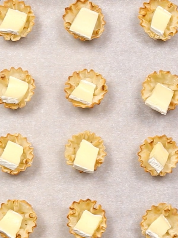 An overhead image of phyllo cups with brie in them spread on a parchment lined baking sheet.