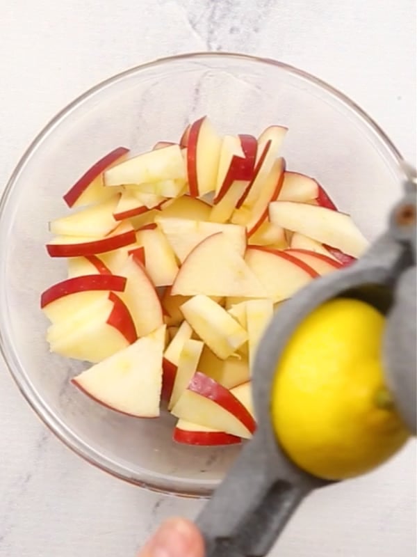 An overhead image of a bowl of SnapDragon Apple pieces with a half lemon being squeezed over them.