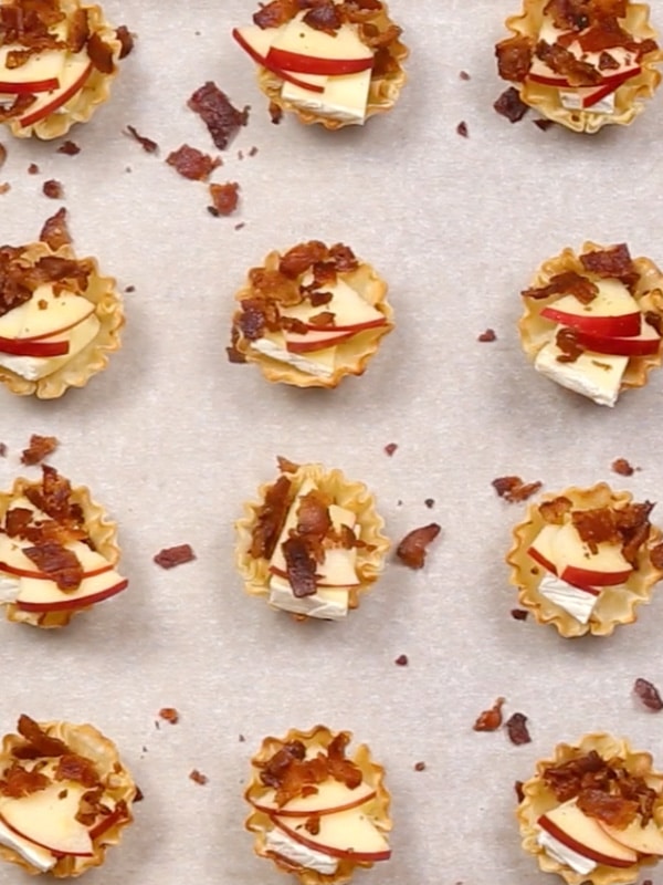 An overhead image of phyllo cups with crumbled bacon added in them spread on a parchment lined baking sheet.