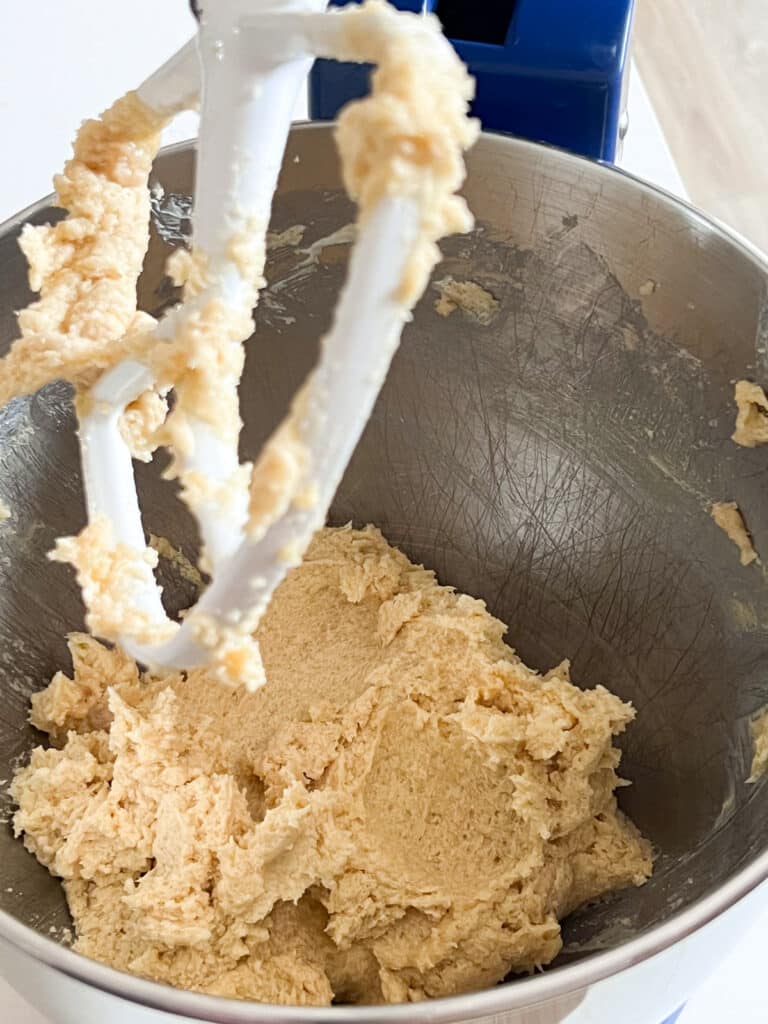 An image of wet ingredients of cookie dough once eggs were added in the bowl of a stand mixer.