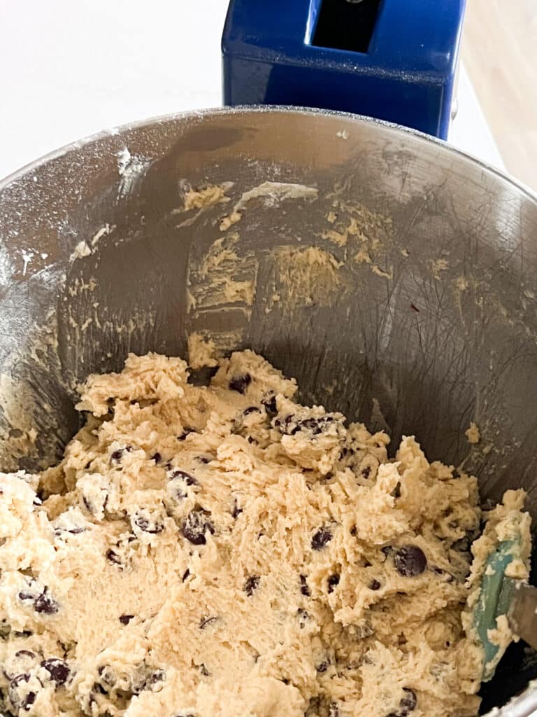 Image of cookie dough in the bowl of a stand mixer after the chocolate chips have been added.