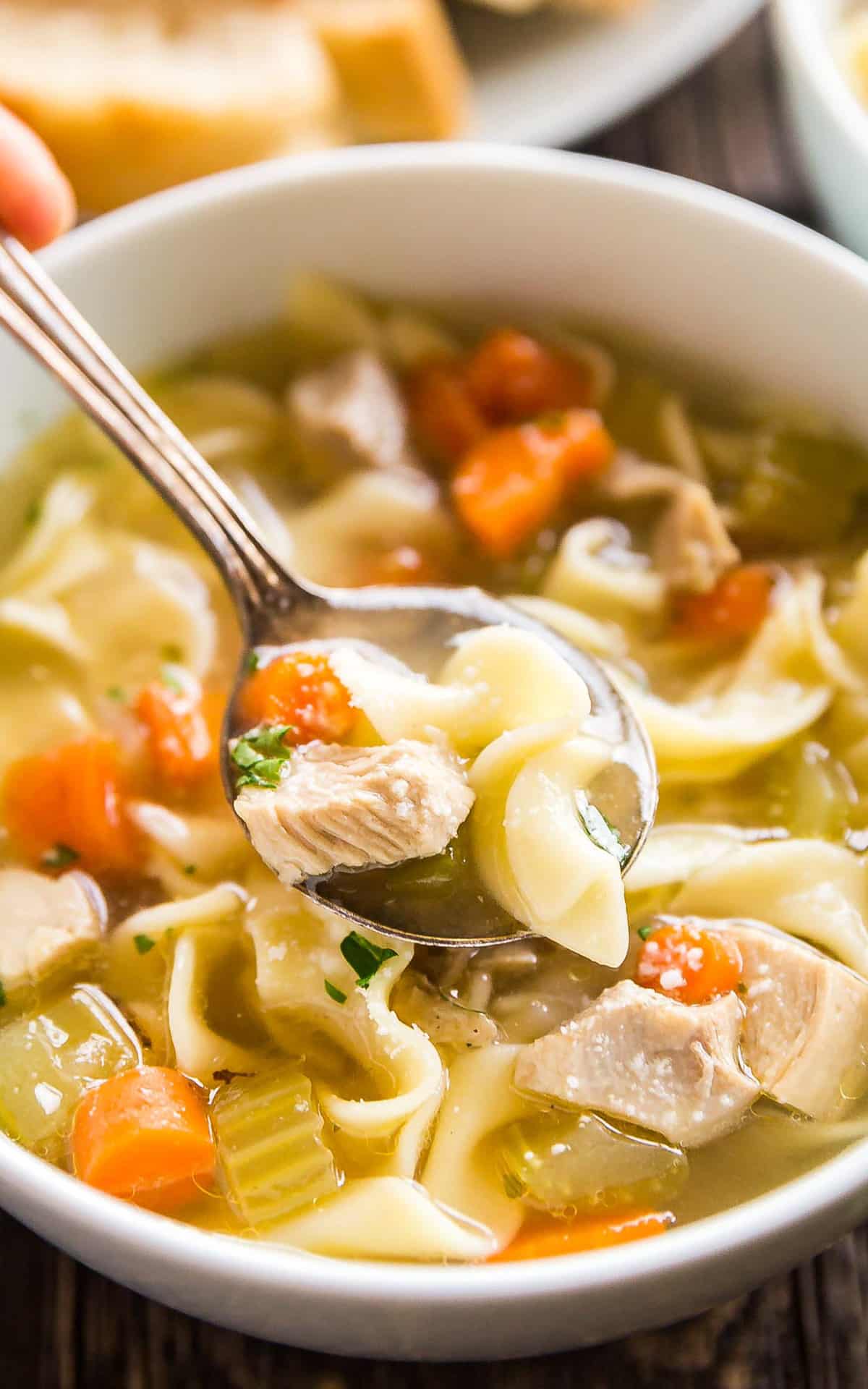 A close up of a spoonful of chicken soup being held over the bowl.