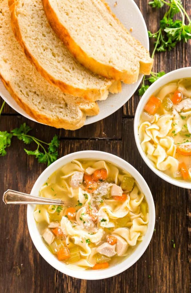 An overhead image of a bowl of chicken pasta soup with sliced bread.