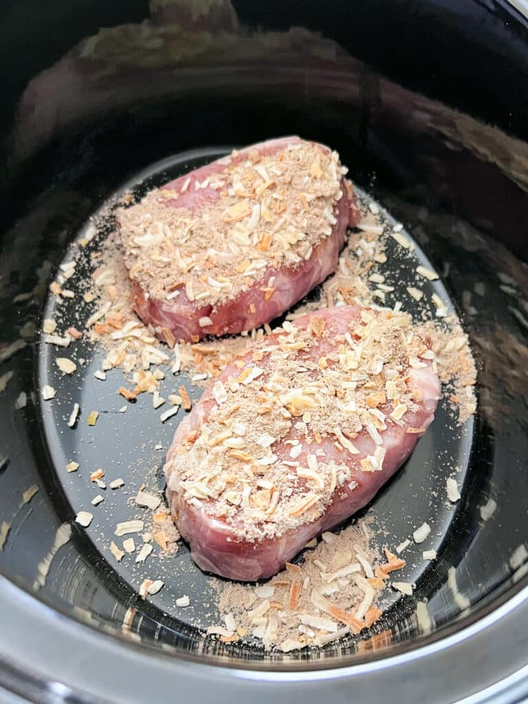 Boneless pork chops in a slow cooker with onion soup mix sprinkled over them.