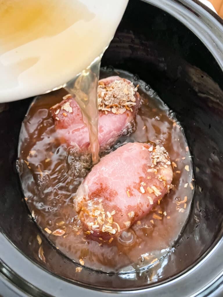 Broth being poured over pork chops in a crockpot.