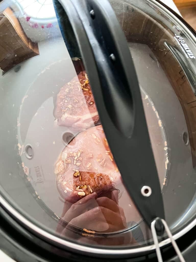 Pork chops in a slow cooker with the cover on it.