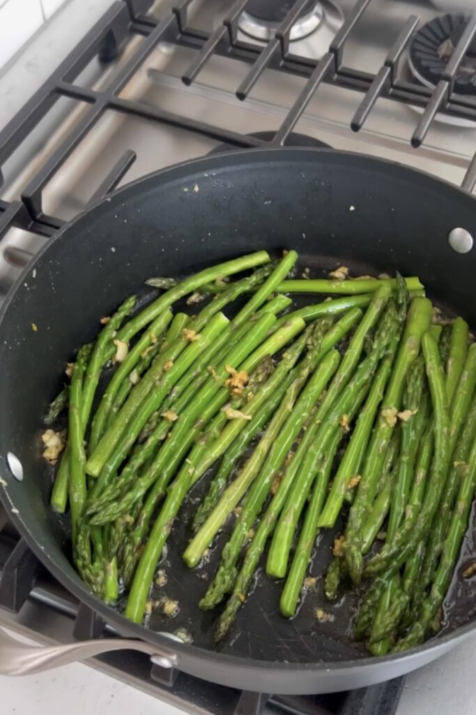 An image of asparagus and garlic cooking in a skillet.