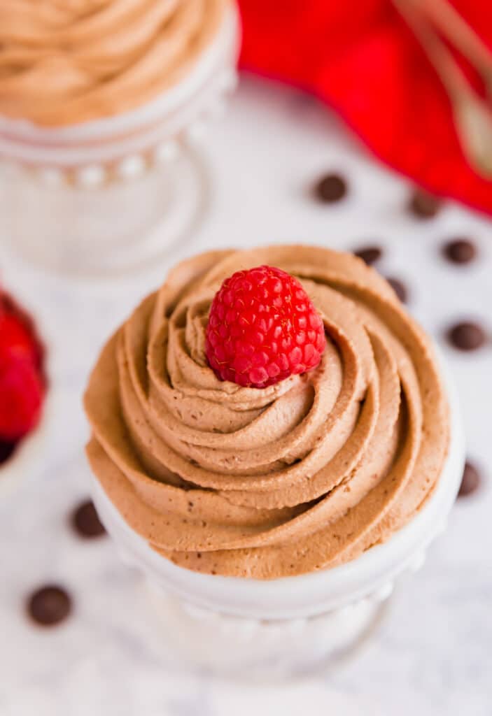 A close up image of the top of a chocolate mousse cup featuring the swirl of mousse topped with a raspberry