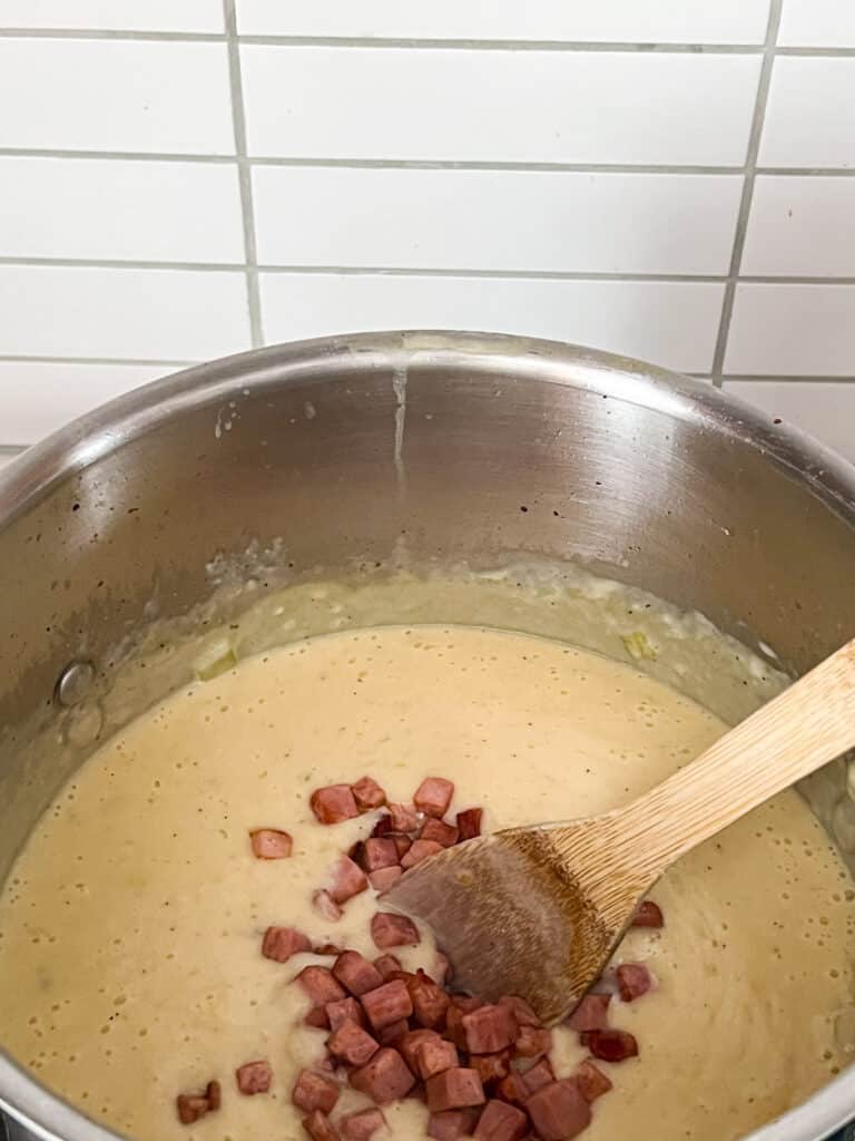 Ham being stirred into the soup in a pot on the stove.