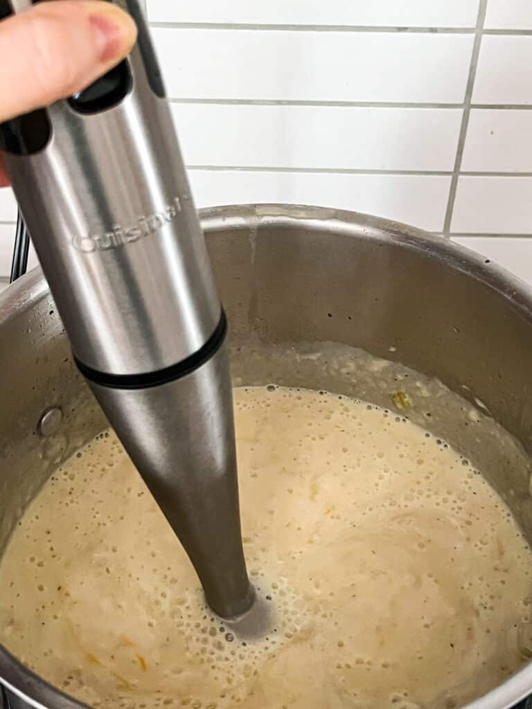 An immersion blender in the pot blending the soup.