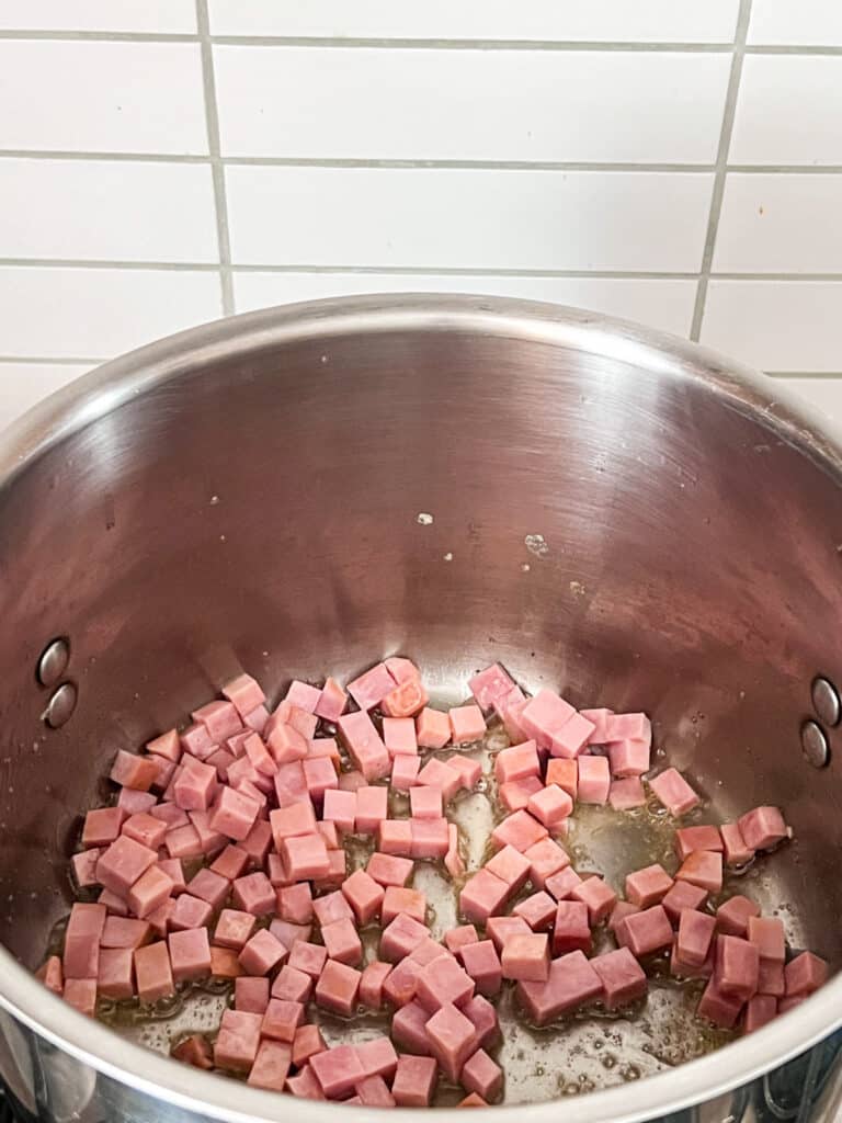 Diced ham in a pot cooking on a stove.