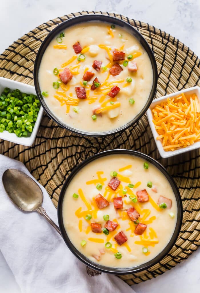 An overhead image of two bowls of this  potato ham soup recipe with garnishes around it.