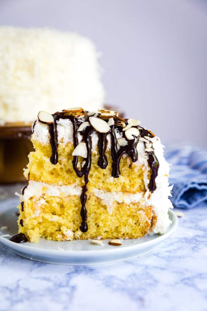 A slice of coconut cake drizzled with chocolate sauce.