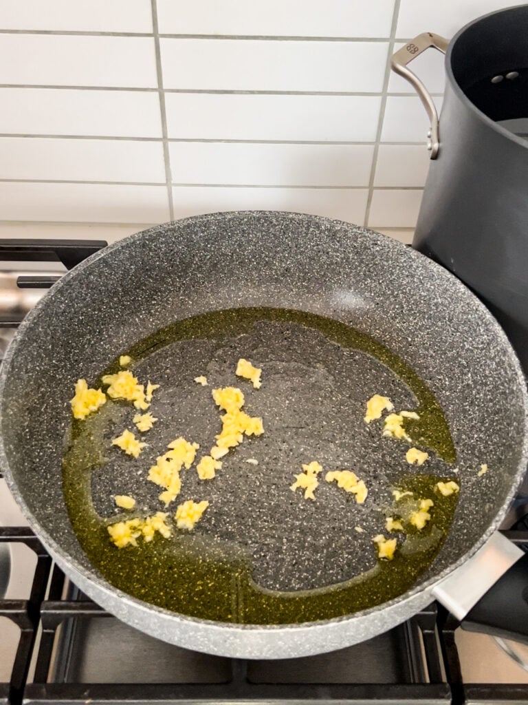 A pan on a stove with sautéed garlic and oil.