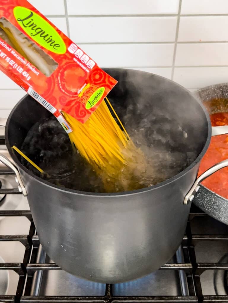 Linguine pasta being poured into a pot of boiling water on a stove.