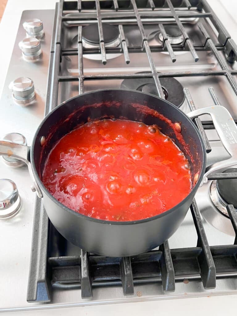 Bubbling pizza sauce simmering in a pot on the stove.