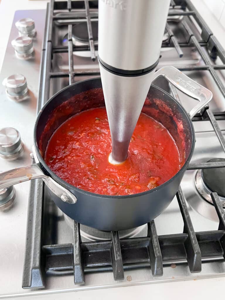 An immersion blender in the pot of sauce pureeing it.