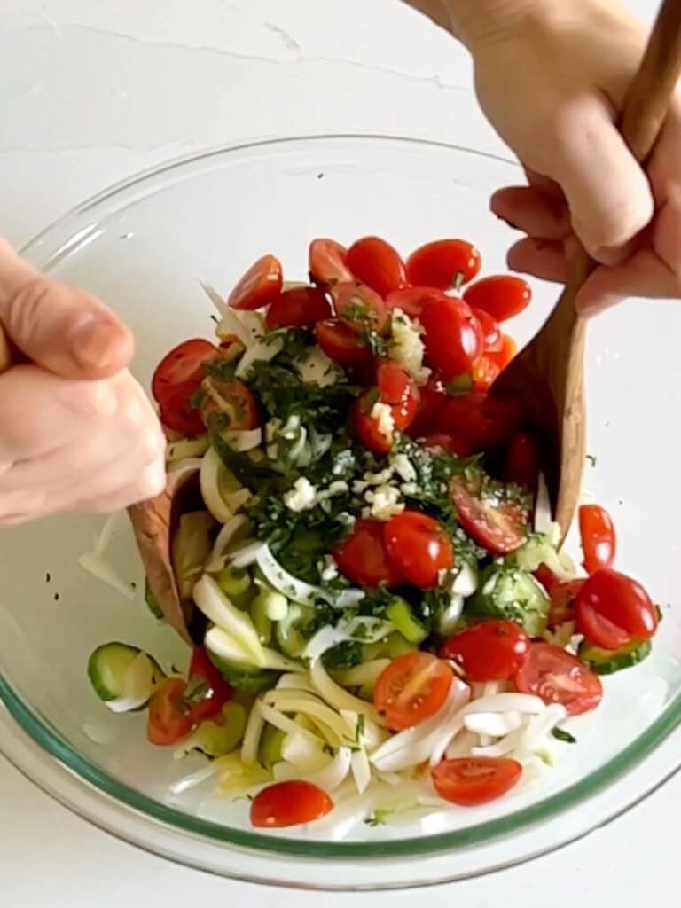 Hands tossing the salad in a large glass bowl.