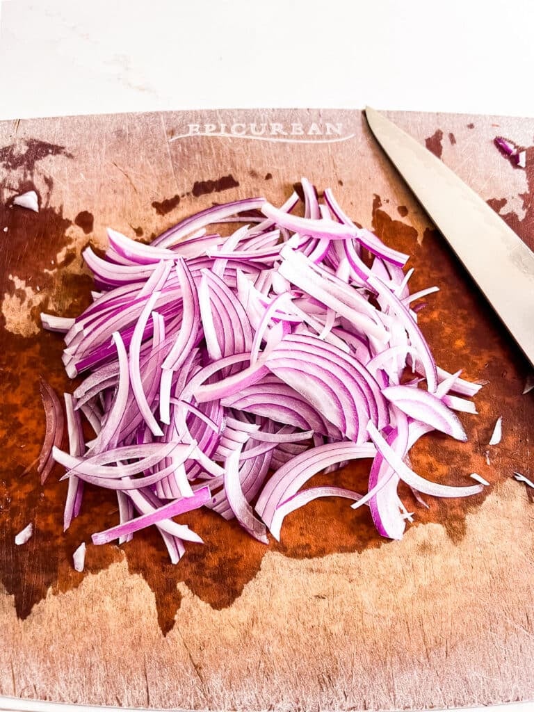 Sliced red onion on a cutting board with a knife.
