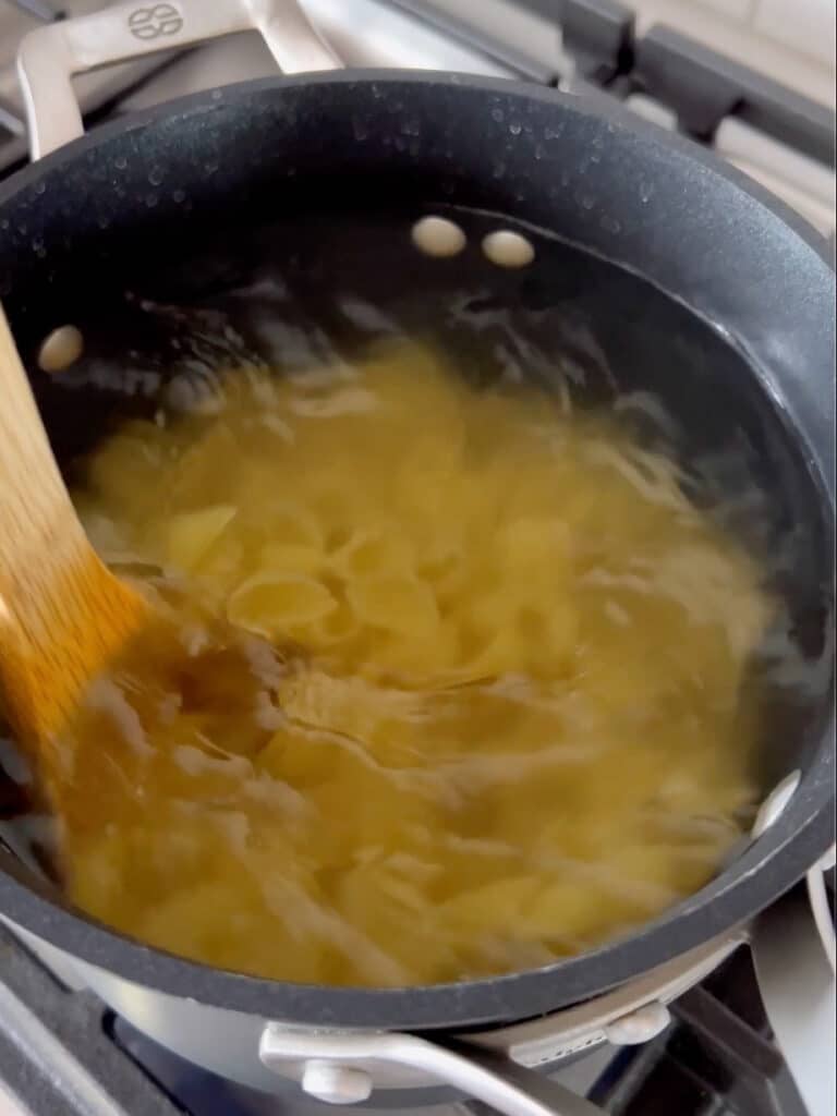 Shell pasta being stirred in a pot of boiling water on a stove.