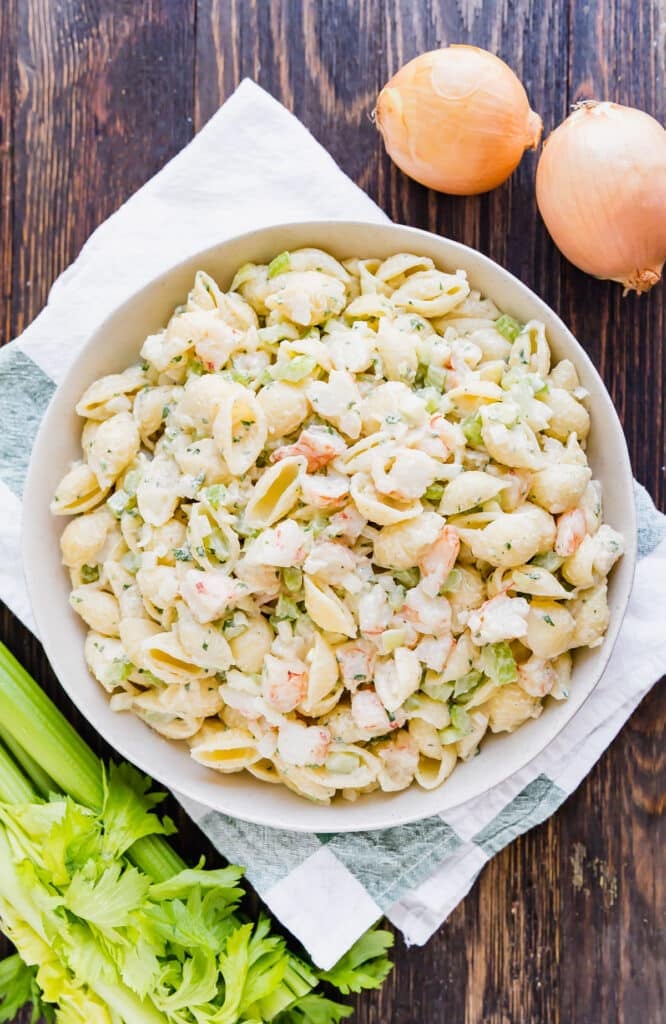 An over head image of a bowl of Shrimp Macaroni Salad with celery and onions around it.