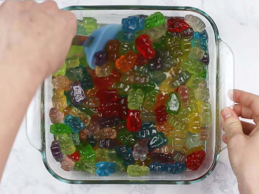 Hands stirring the vodka gummy bears with a blue spatula.