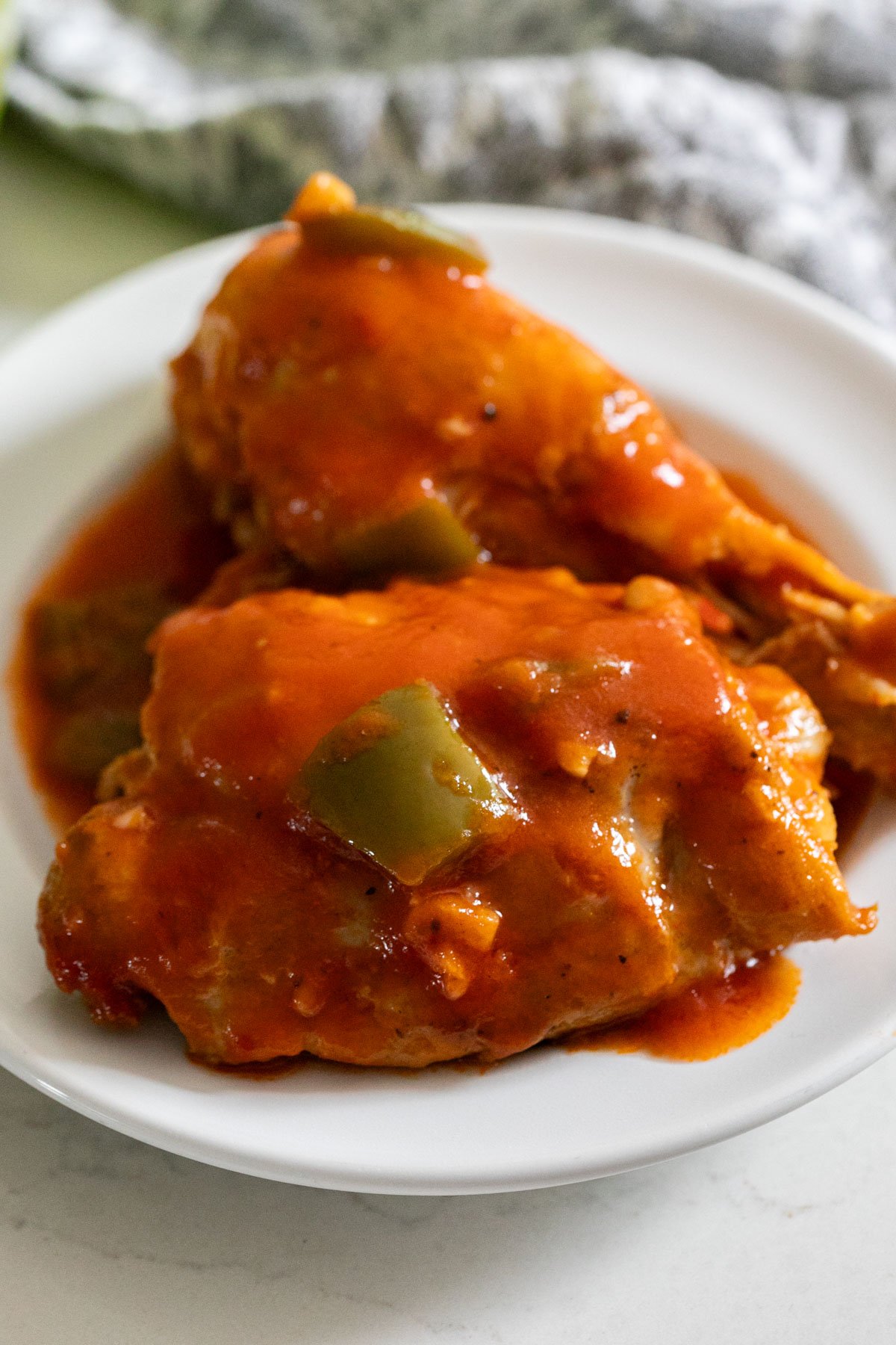 A close up image of chicken with tomato sauce and green peppers on a plate.