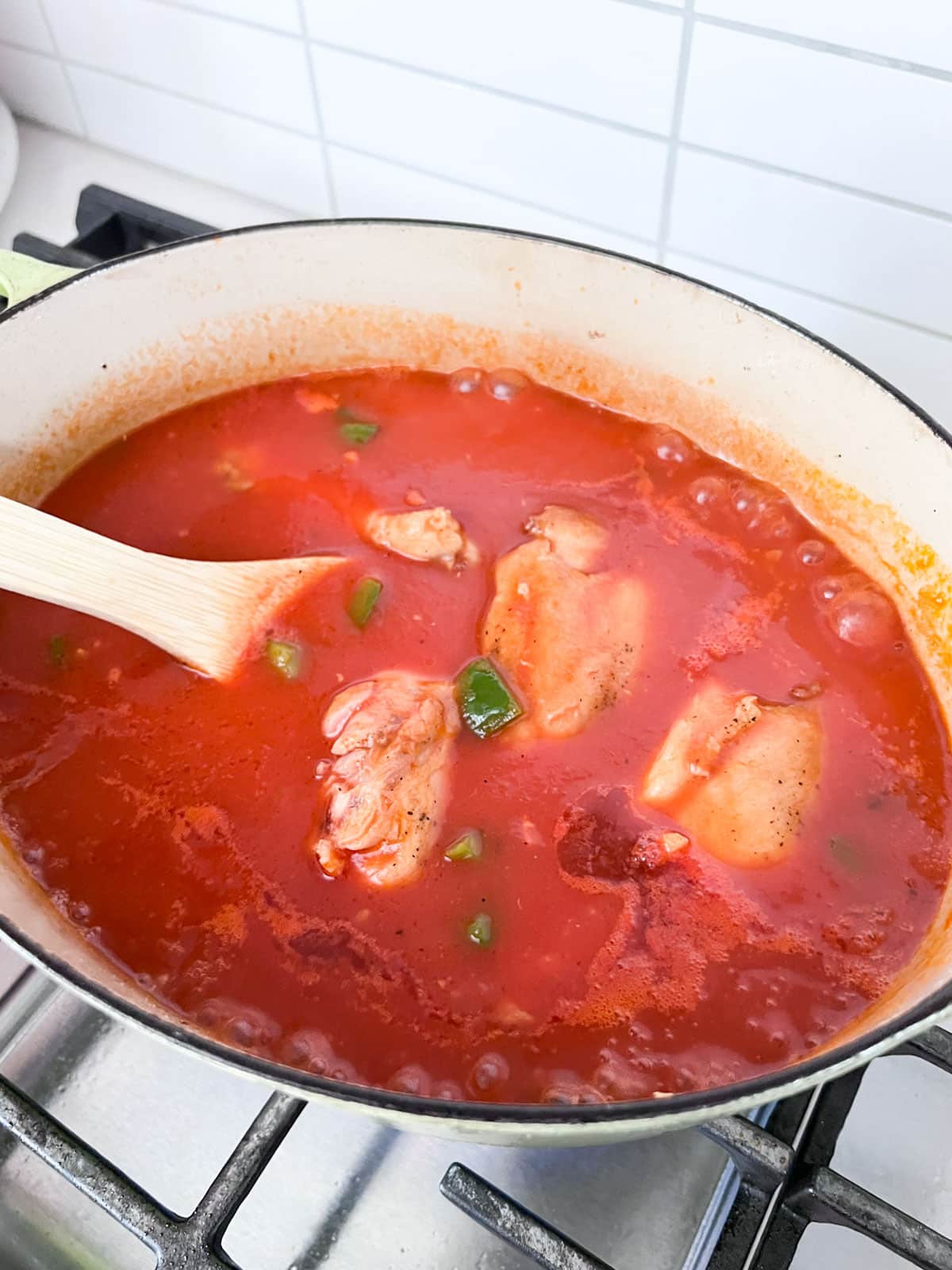 Chicken simmering in tomato sauce with peppers in a dutch oven.