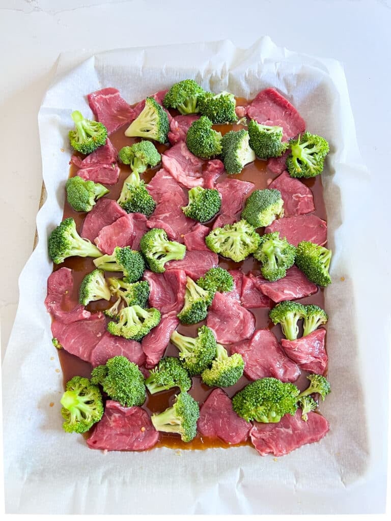 Steak slices, broccoli and sauce on a parchment lined sheet pan.