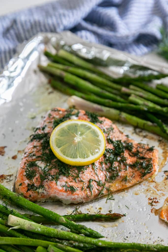 Salmon and asparagus on a foil lined sheet pan with a blue and white striped napkin behind it.