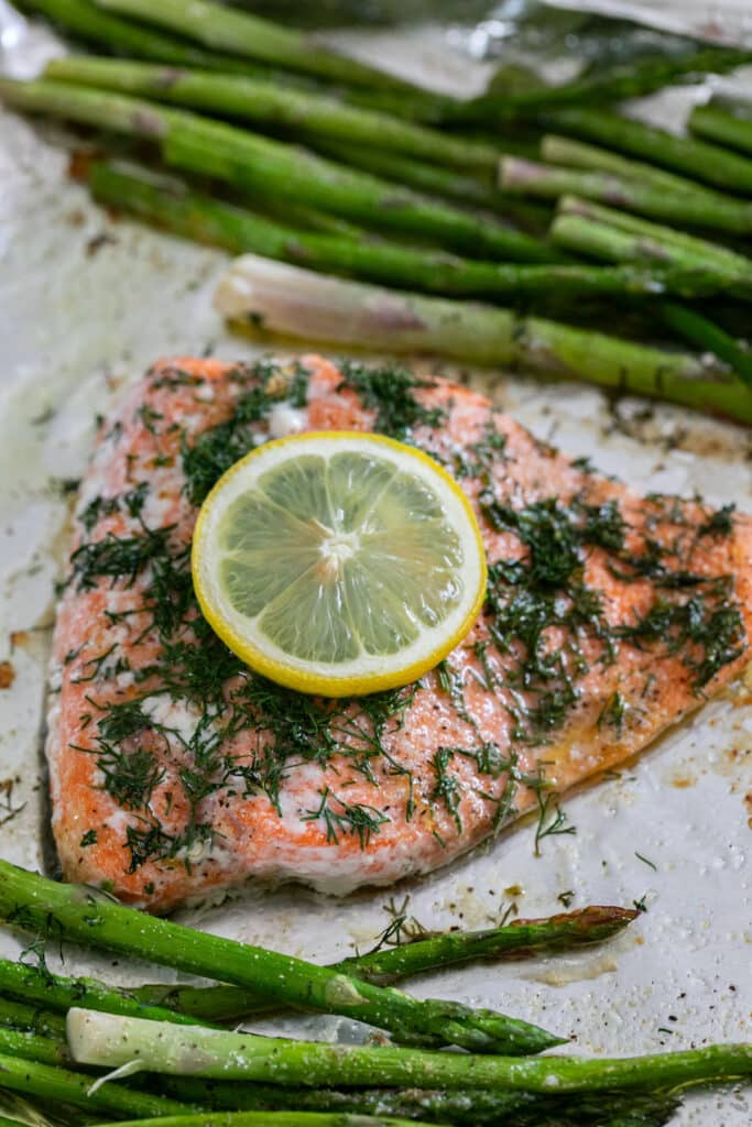 A close up of a piece of dill salmon on a pan with asparagus next to it.