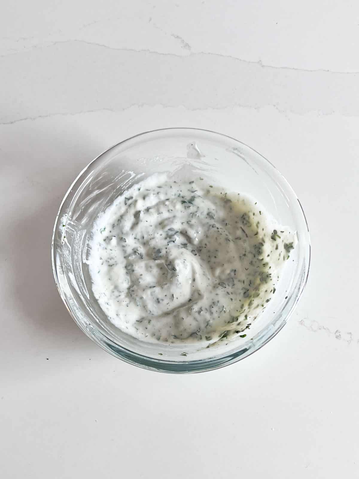 A glass bowl of herbed yogurt.