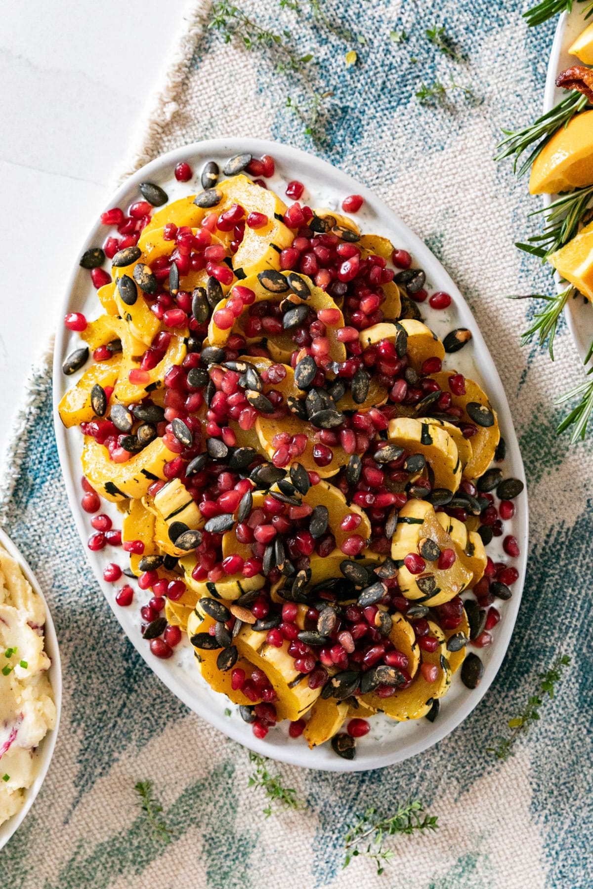 Overhead image of delicata squash with pomegranate arils and pepitas on an oval plate.