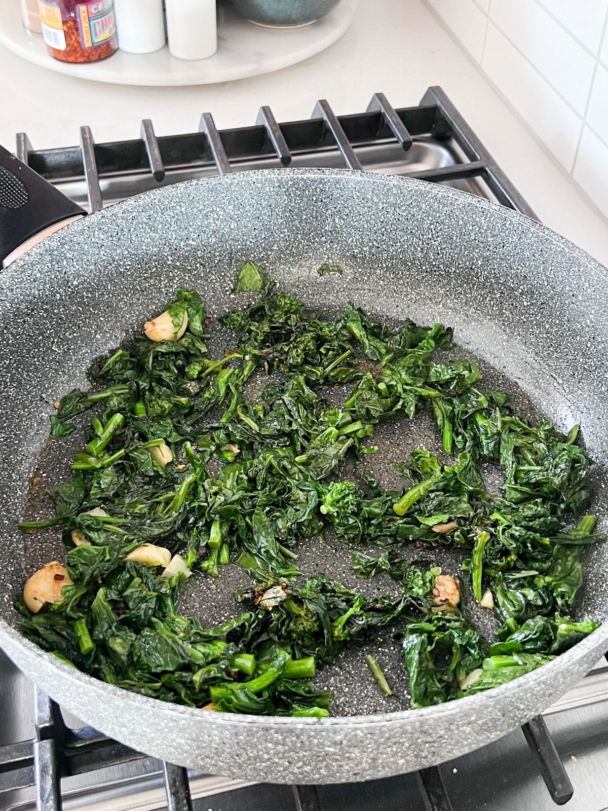 A skillet on a stove with the broccoli rabe cooked down in it.