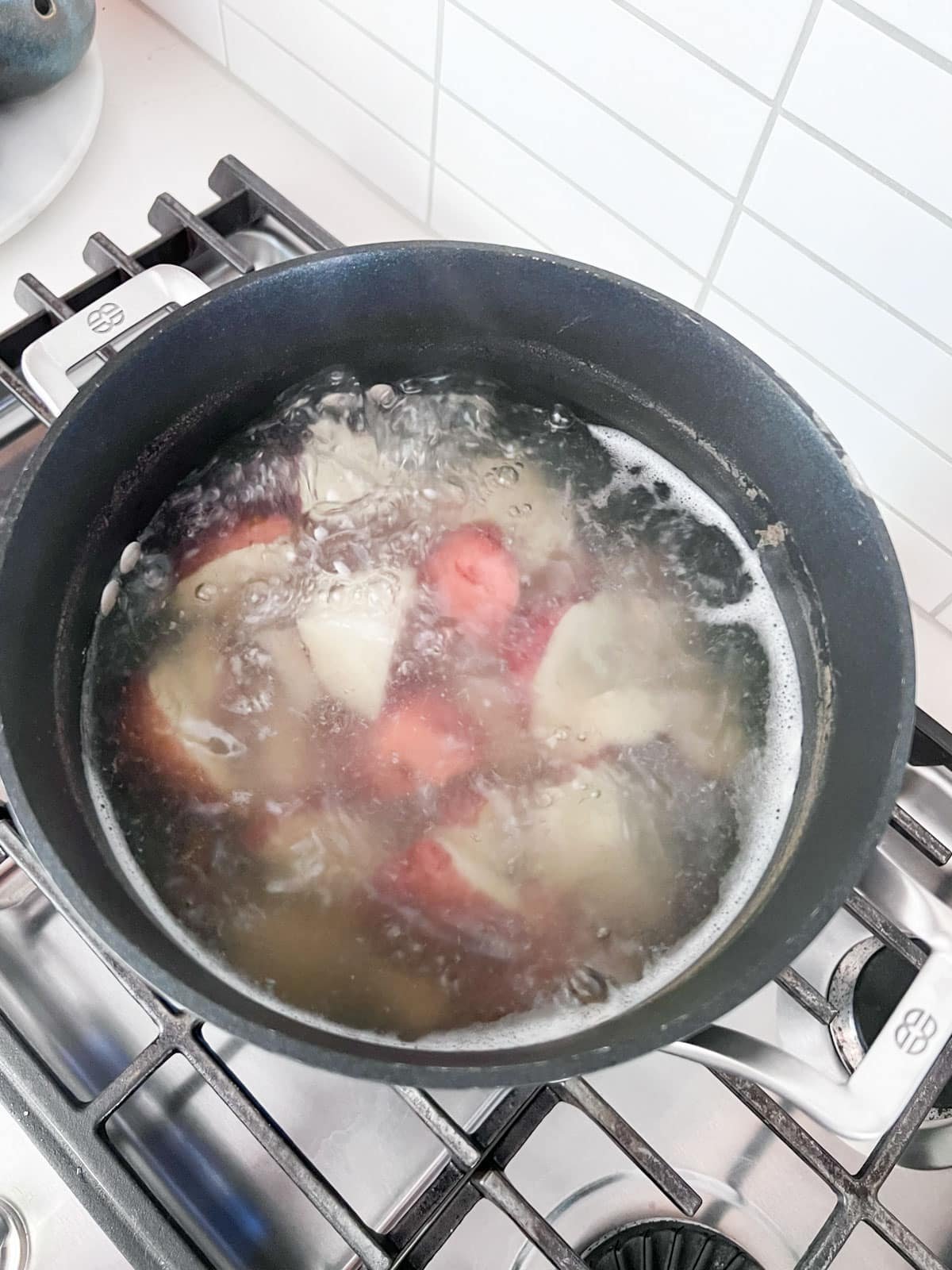 Potatoes boiling in a pot on a stove.