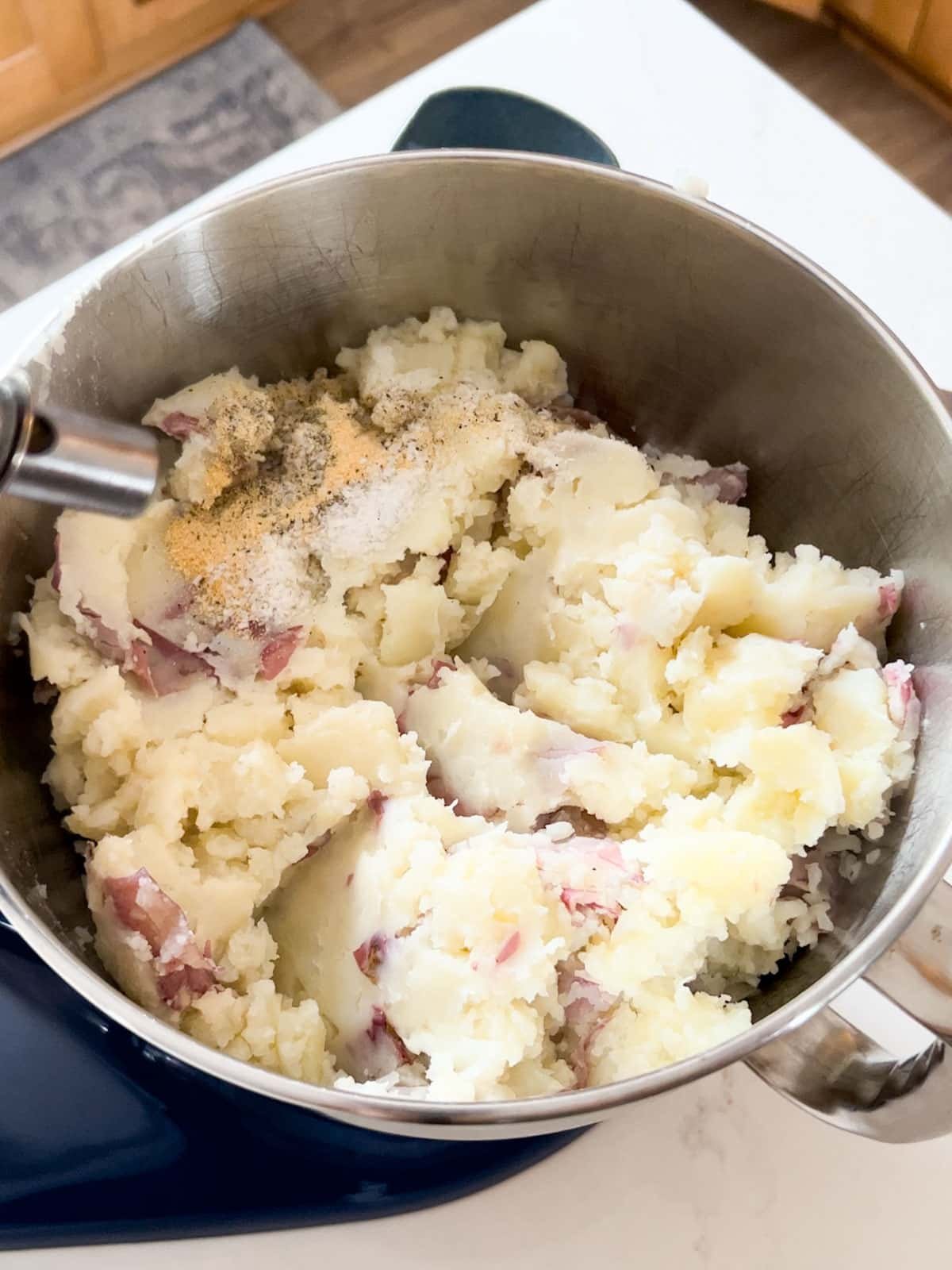 Partially mashed potatoes in stand mixer bowl with other ingredients ready to finish being mashed.
