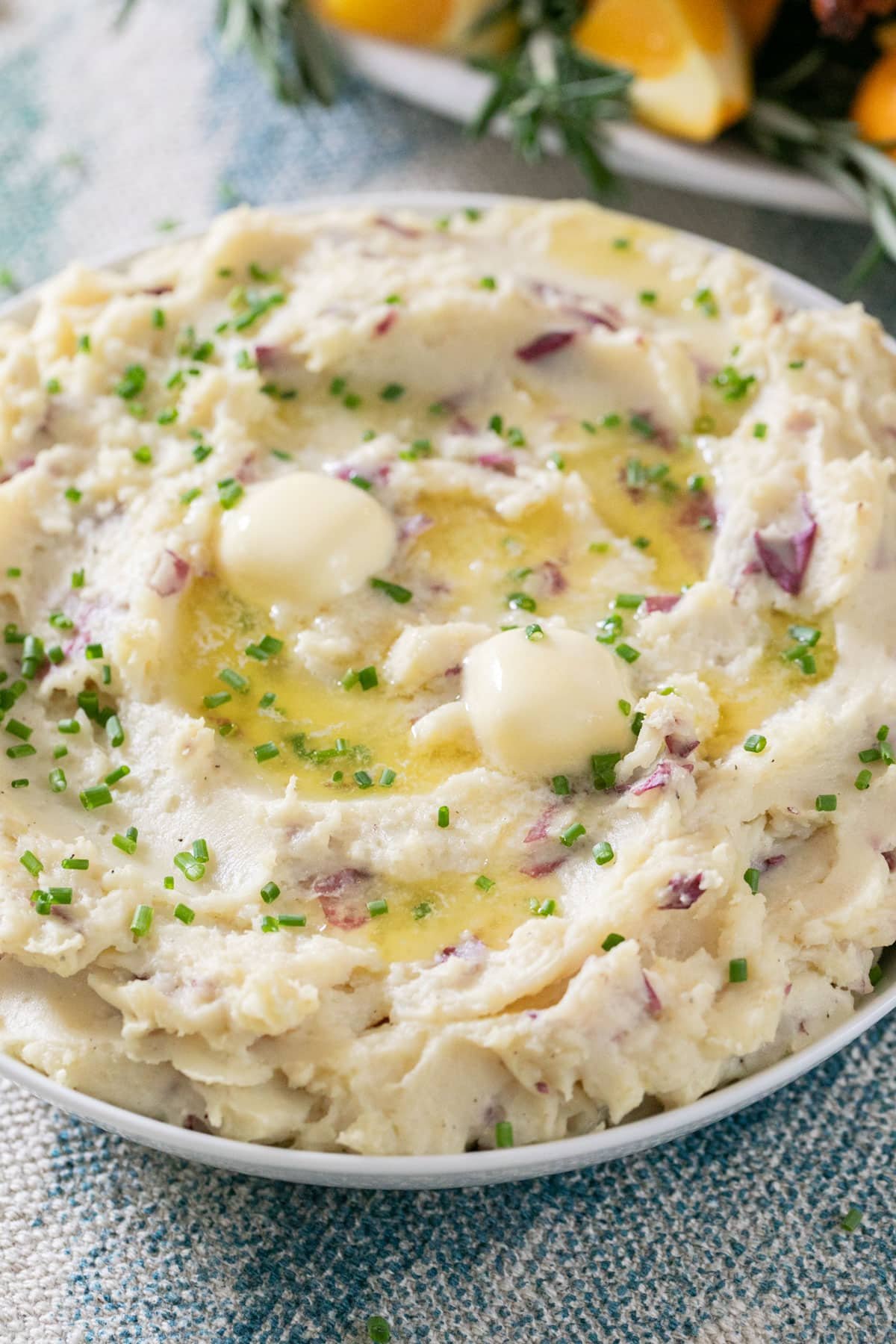A close up image of mashed potatoes with butter and chives in a white bowl.