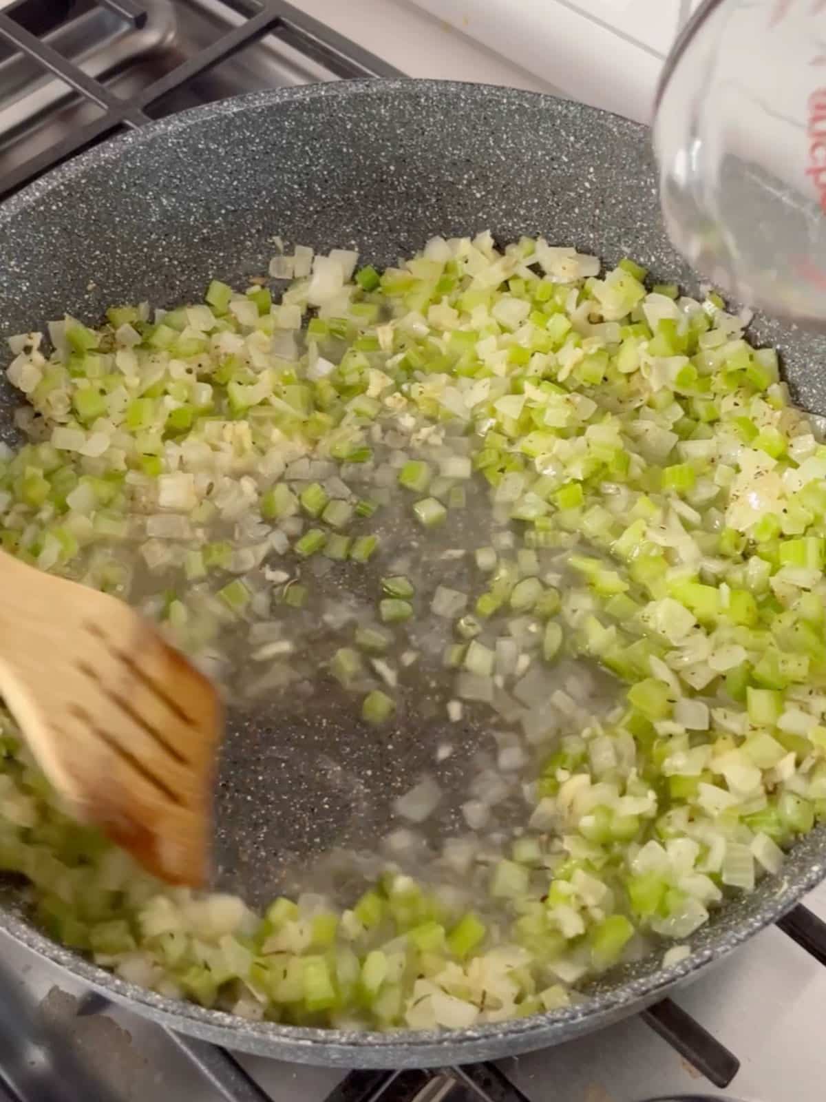 A wooden spoon deglazing the pan of celery and onion with white wine.