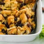 The corner of Italian bread stuffing in a white casserole dish with a spoon in it.