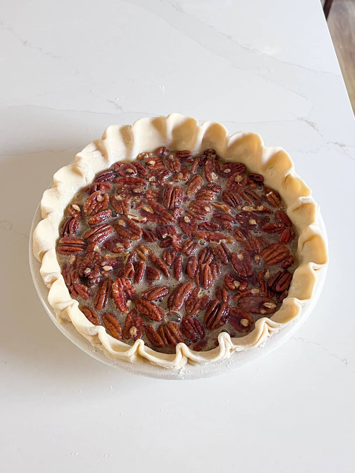 Raw pie crust with pecans and filling in it.