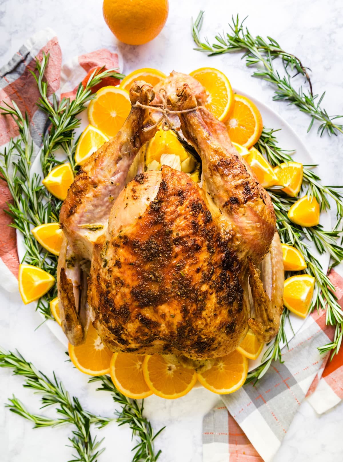 An overhead image of a whole turkey on a platter with rosemary and oranges.