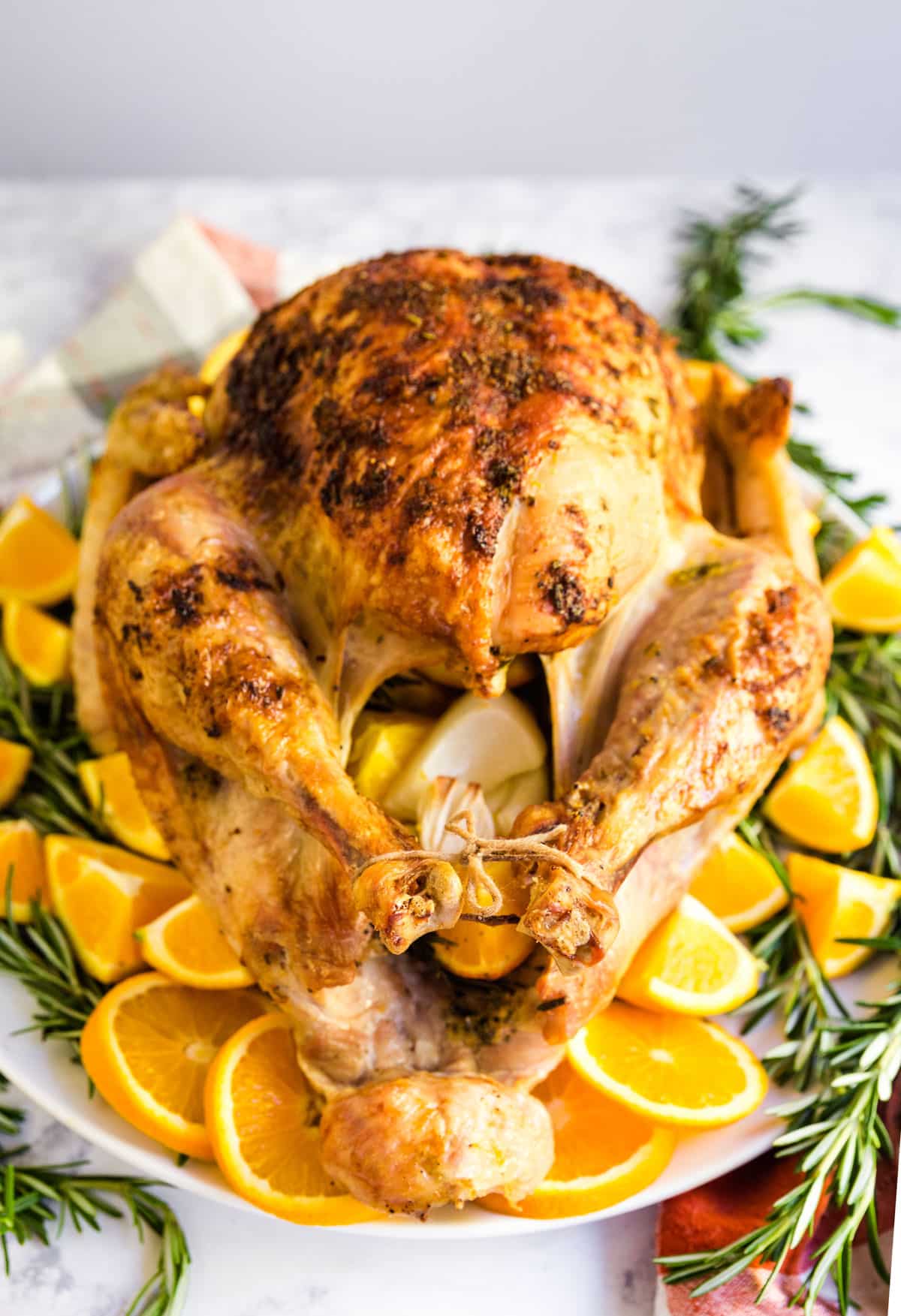 A whole turkey on a platter atop oranges and rosemary.