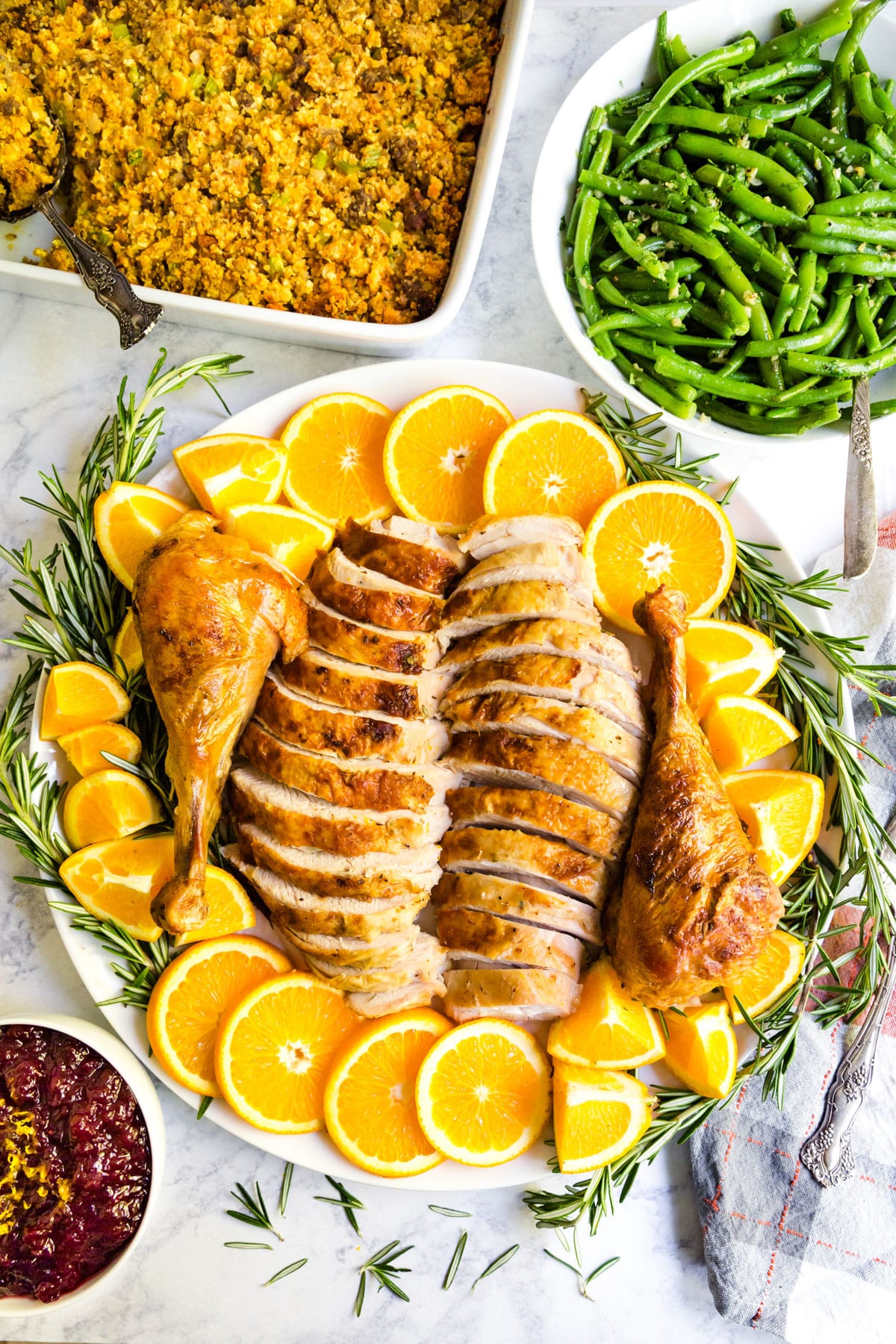 An overhead image of a thanksgiving table with the platter of carved turkey in the middle and green beans, dressing and cranberry sauce around it.