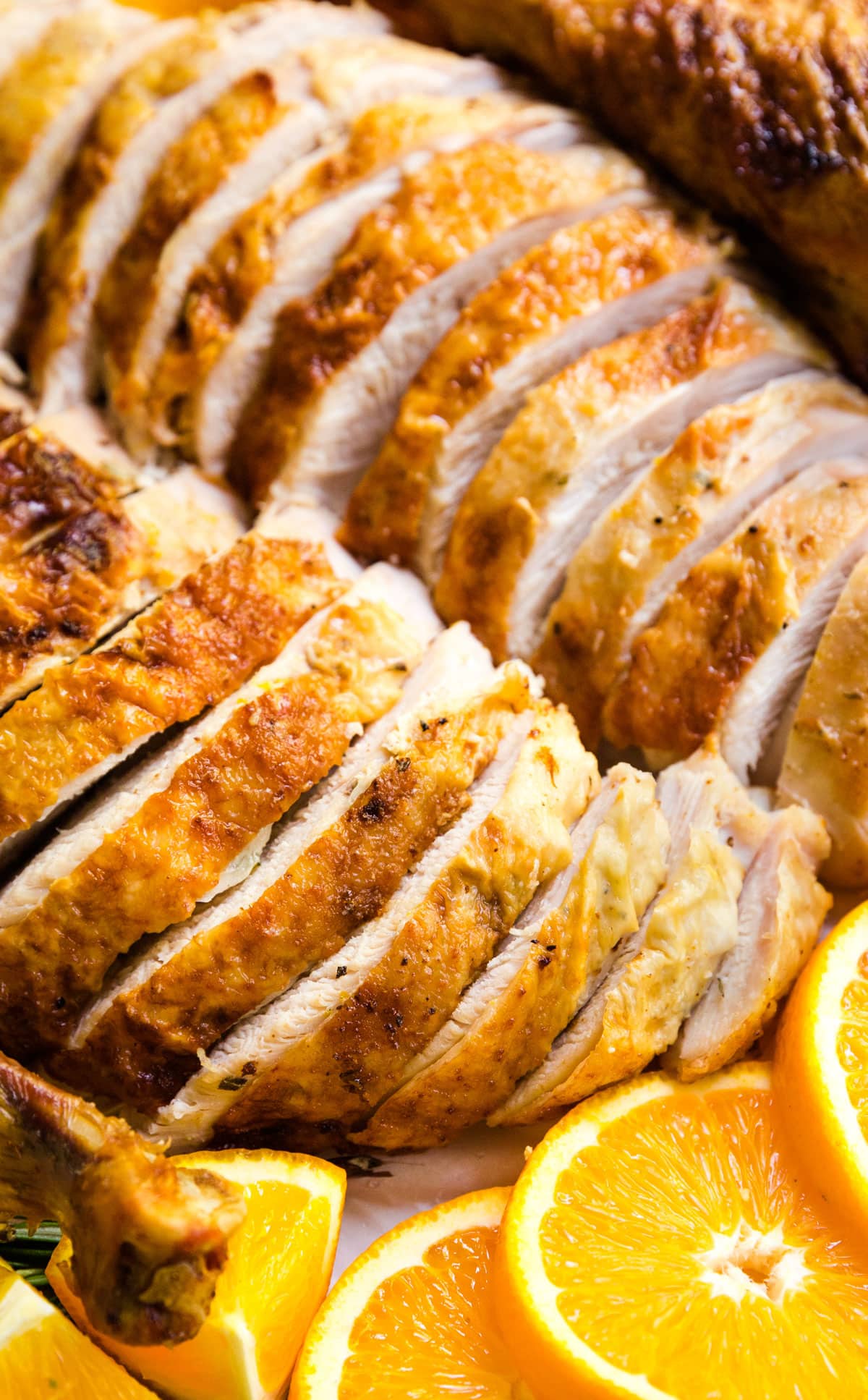 A close up image of juicy, perfectly sliced turkey with orange slices next to it.