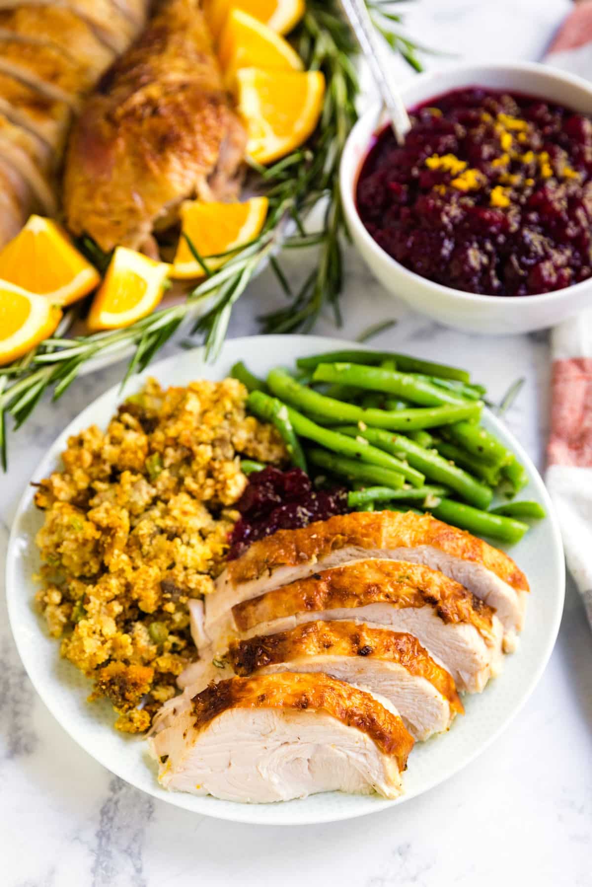 A plate of turkey, dressing and green beans with cranberry with the whole bird and cranberry sauce behind it sauce.
