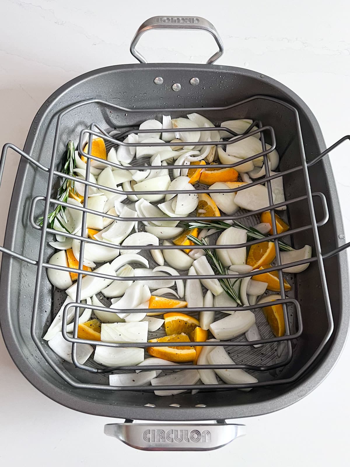 The prepared turkey pan of onions and oranges with a metal rack in it.