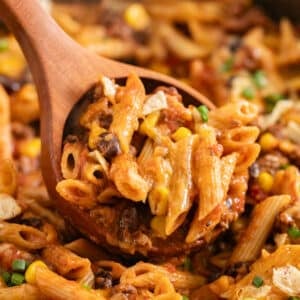 A wooden spoon scooping up creamy taco pasta from the pan.