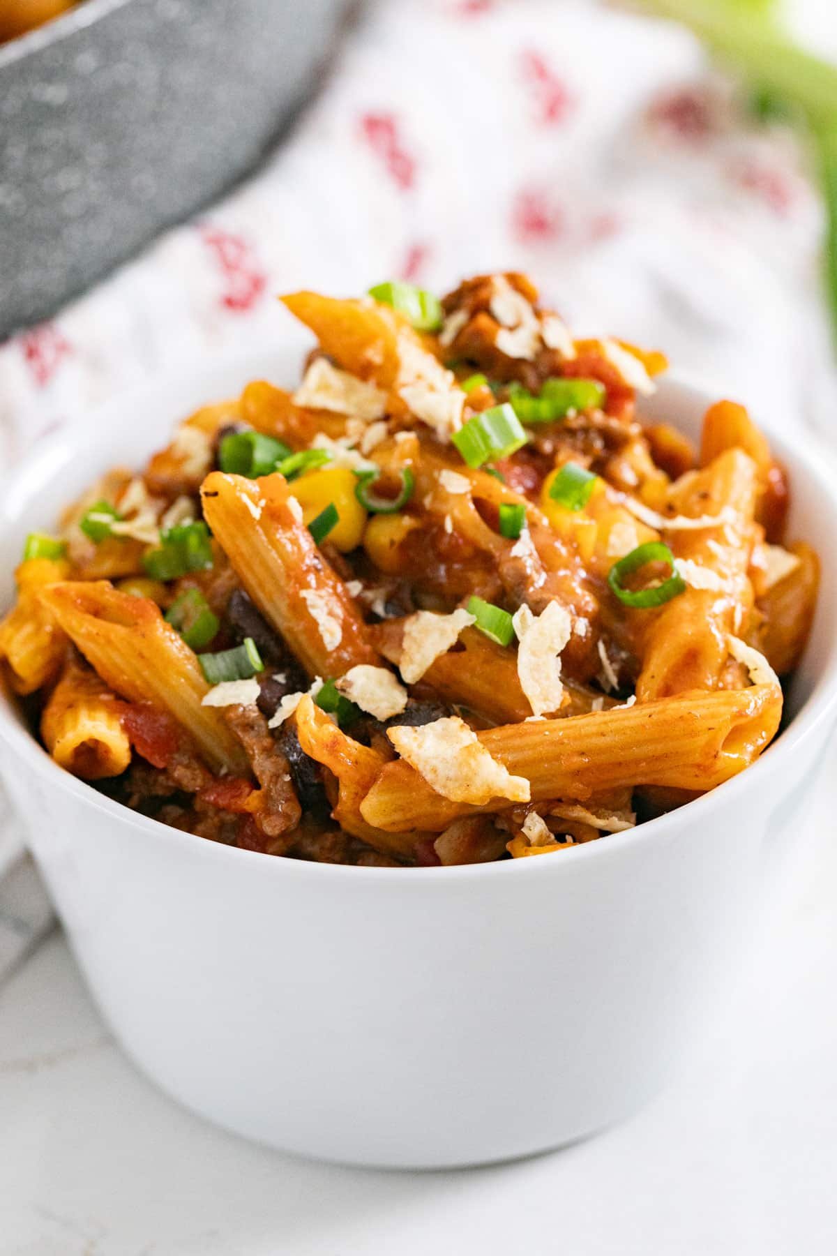 A close up image of a bowl of taco pasta with crushed chips and green onion on top.