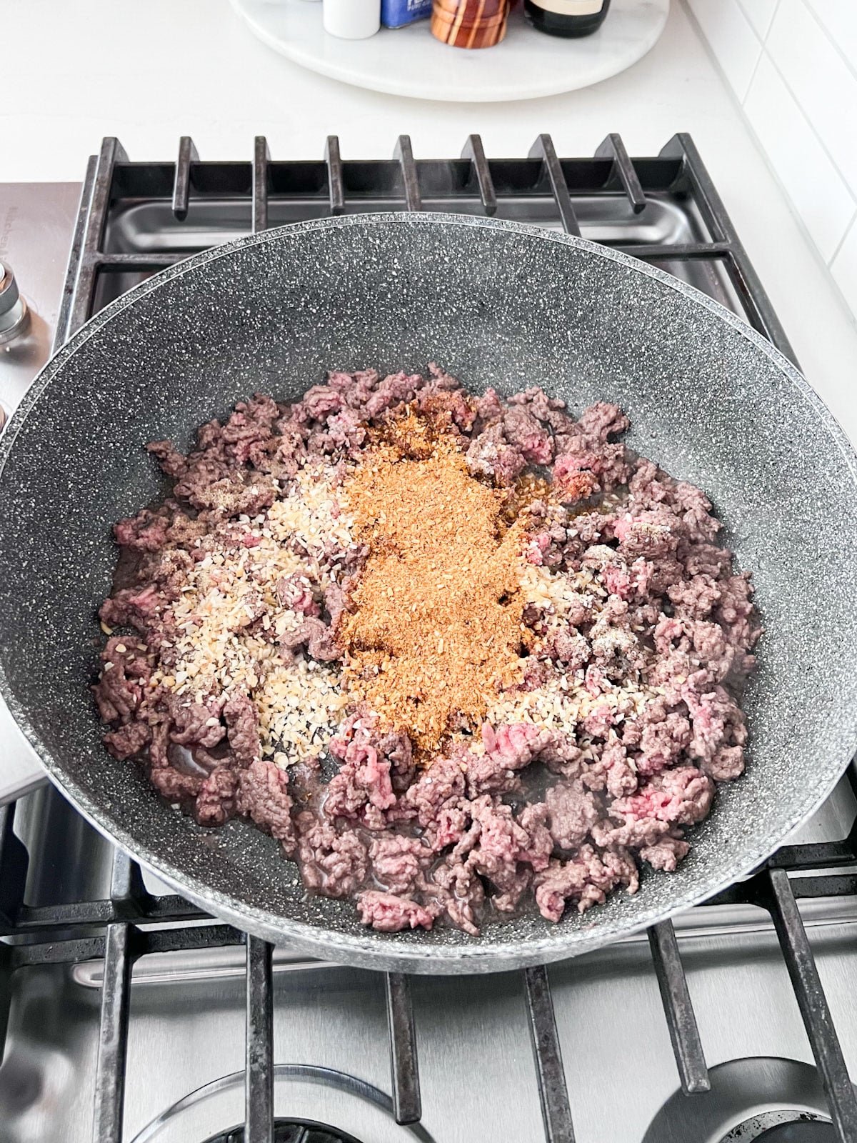 Browning ground beef and seasoning in a skillet on a stove.
